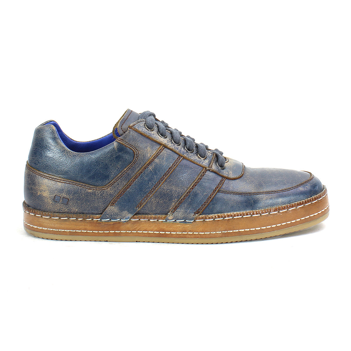 The Bed|Stü Firepower is a blue leather everyday sneaker featuring a brown textured sole, decorative stitching, leather stripe accents, and laces, displayed in a left side profile view against a white background.