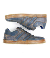 A side view of the Bed|Stü Firepower sneakers—a pair of distressed blue leather shoes featuring tan textured soles and three leather stripe accents on the side.