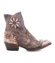 The Bed|Stü Frio is a brown leather Western bootie featuring decorative stitching, floral cutouts, antiqued brass studs, and a low heel, shown in profile against a white background.