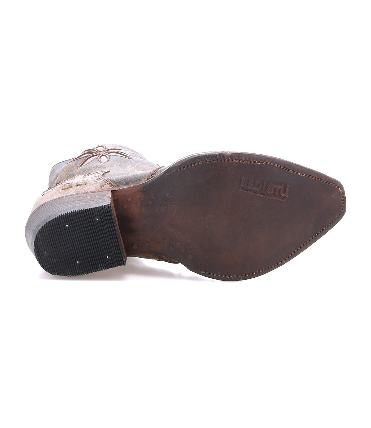 The Frio bootie from Bed|Stü is showcased sole-up, highlighting its pointed toe, intricate stitch details, nailhead accents on the heel, and the "Bed|Stü" logo embossed on the leather outsole. Subtle floral cutouts and antiqued brass studs lend distinctive flair to this striking Western-inspired design.
