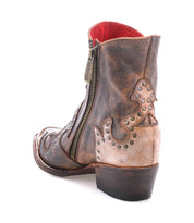 Frio by Bed|Stü: A distressed leather Western bootie ankle boot featuring decorative stitching, floral cutout detailing, antiqued brass studs, and a side zipper, displayed from the rear angle on a white background.