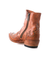 The Frio bootie by Bed|Stü features brown leather with decorative stitching, antiqued brass studs, a side zipper, and a low stacked heel, shown against a white background.