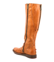 The Bed|Stü Glaye boot is a tall brown leather equestrian style featuring a side zipper, low heel, rounded toe, and a classic vintage buckle for added charm—elegantly displayed against a white background.