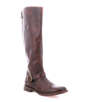 The Glaye by Bed|Stü is a brown leather knee-high equestrian boot featuring a low heel, vintage buckle strap at the ankle, and side zipper, displayed against a white background.