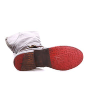 A tall Bed|Stü Glaye leather boot lies on its side, displaying the sole with a distinct red section at the toe and a textured tread pattern.