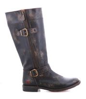 The Bed|Stü Gogo Lug is a tall, distressed black leather engineer boot with two brass buckles and a side zipper, featuring a rugged lug outsole, shown from the side against a white background.