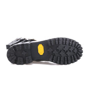 Close-up of the Bed|Stü Grab boot’s rugged black rubber sole with deep treads and a yellow Vibram logo at the center, showcasing studded buckle straps along the upper for added edge.