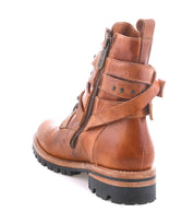 The Bed|Stü Grab is a brown leather combat boot featuring a side zipper, back strap detail, visible stitching, and studded buckle straps for added edge, finished with a rugged black Vibram sole. Shown photographed on a white background.