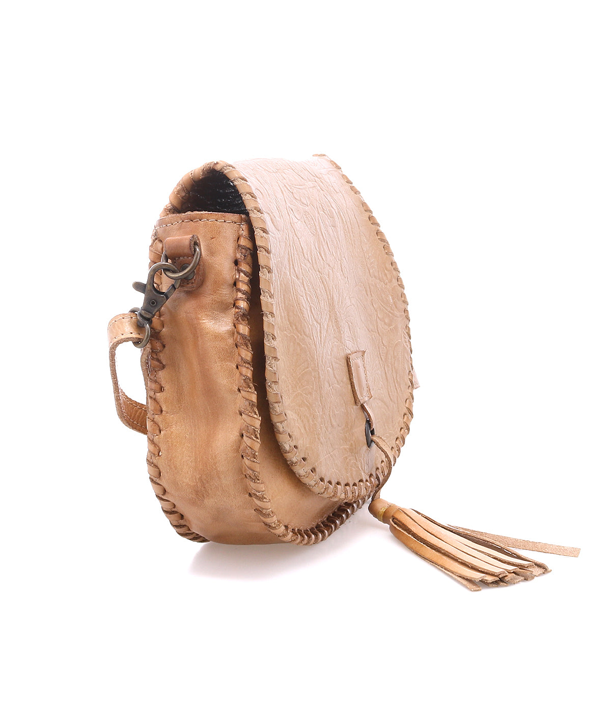 The Bed|Stü Half Moon EM is a tan leather saddlebag crossbody purse featuring stitched edges, an embossed foliage pattern, and a flap closure. It is detailed with a side buckle and bottom tassel, and includes an adjustable strap for versatile wear.