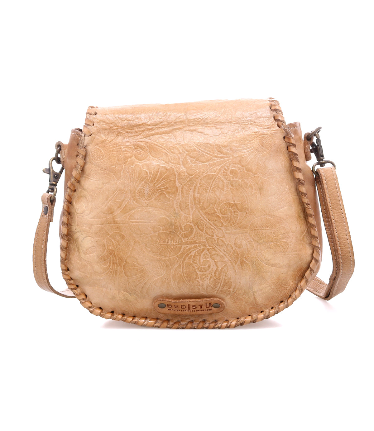 The Bed|Stü Half Moon EM is a light brown leather saddlebag crossbody purse featuring an embossed foliage pattern, whipstitch trim, and adjustable strap, displayed on a white background.