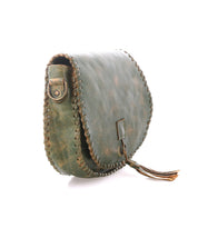 The Bed|Stü Half Moon is a green leather tassel bag featuring hand-laced stitching along the edge, a metal button closure, and an adjustable strap, shown on a white background.