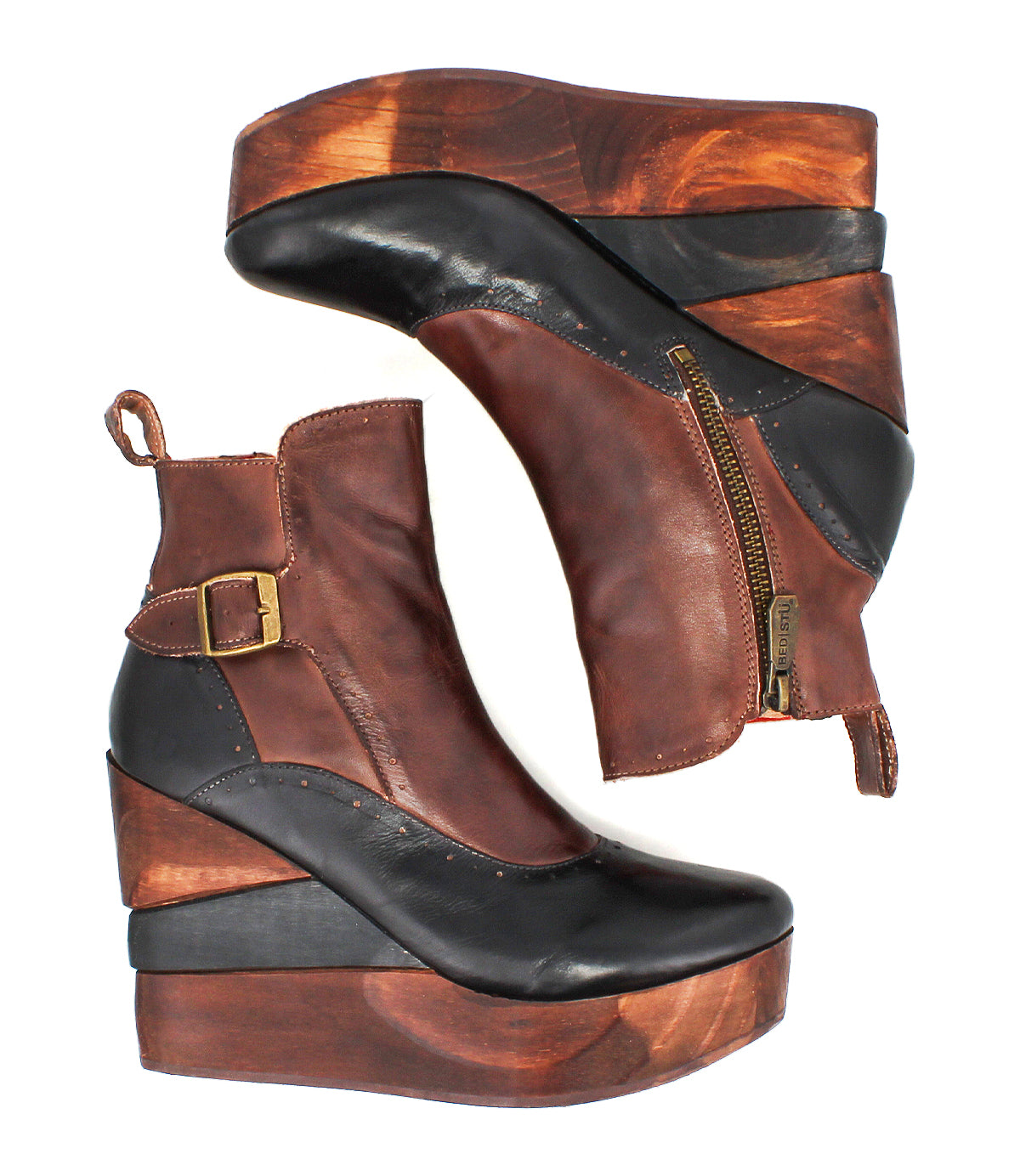 Pair of Bed|Stü Harmonious brown and black leather wedge ankle boots, featuring leather uppers, sculpted wood base soles, side zippers, and brass buckles, laid on a white background.