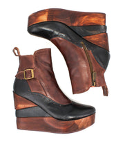 Pair of Bed|Stü Harmonious brown and black leather wedge ankle boots, featuring leather uppers, sculpted wood base soles, side zippers, and brass buckles, laid on a white background.