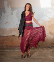 A woman poses indoors against a weathered wall and brick background, wearing a maroon lace dress and Bed|Stü Harmonious platform wedge ankle boots with leather uppers, holding the skirt of her dress and a black jacket.