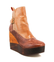 The Bed|Stü Harmonious is a platform wedge ankle boot with brown and tan leather uppers, featuring a thick sculpted wood base and a side buckle detail, shown against a white background.