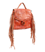 The Bed|Stü Hidden backpack features brown soft leather with a slightly worn texture, fringe detailing on both sides, a top handle, and a flap closure accented by a ring. Its structured silhouette also includes an adjustable crossbody strap for versatile styling.