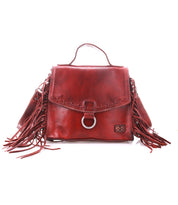 Introducing the Bed|Stü Hidden, a red leather handbag boasting fringe accents on both sides, a sturdy top handle, and a front flap adorned with signature metal ring detailing. Crafted from soft leather with visible stitching and a structured silhouette, this versatile bag also comes with a crossbody strap for effortless carrying.