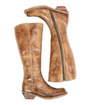 A pair of tall brown leather boots from Bed|Stü, called "Humble," featuring a square-toe boot design, visible side zippers, low stacked heels, and distressed detailing.