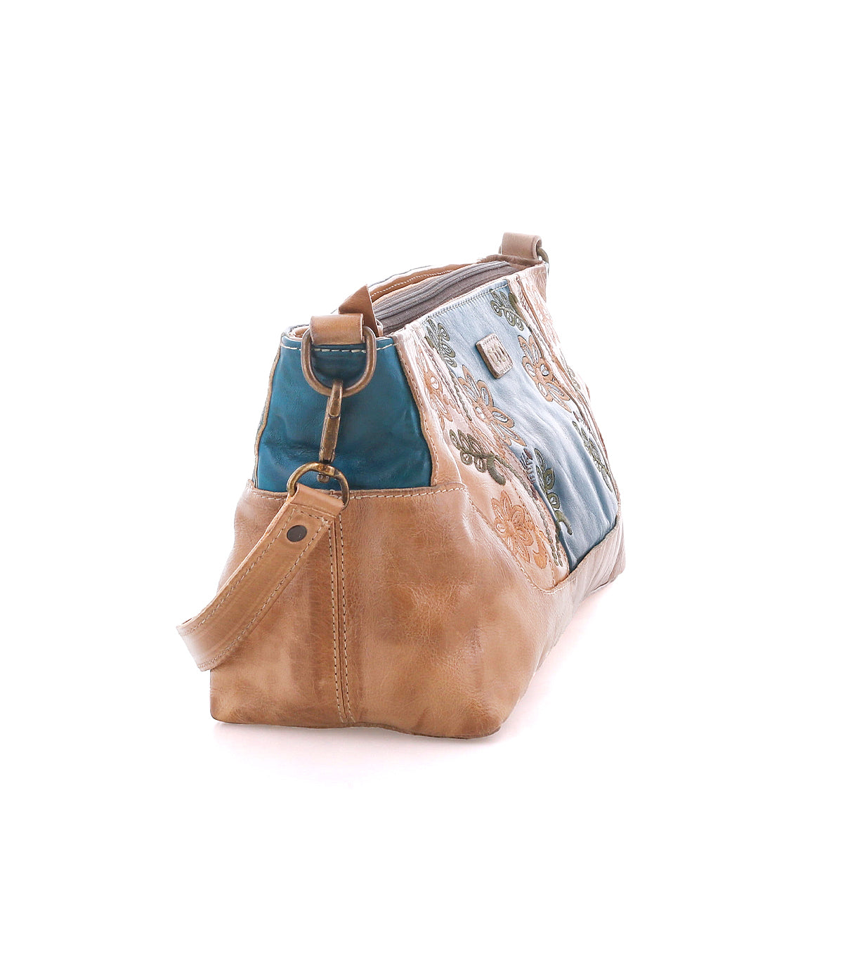 A side view of the Bed|Stü Hyperbolic, a handcrafted leather shoulder bag made with tan leather and blue fabric, adorned with floral embroidery, a shoulder strap, and metal accents, photographed on a white background.