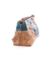 A side view of the Bed|Stü Hyperbolic, a handcrafted leather shoulder bag made with tan leather and blue fabric, adorned with floral embroidery, a shoulder strap, and metal accents, photographed on a white background.