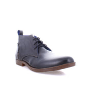 The Bed|Stü Illiad, a single black leather dress shoe featuring a modern lace-up design, brown sole, comfortable outsole, and slight heel, is displayed on a white background.