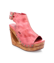 The Imelda by Bed|Stü is a pink open-toe wedge sandal with a cutout wooden platform heel, accented by silver rivet details and adjustable ankle buckles, shown on a white background.