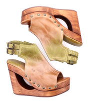 The Imelda sandals by Bed|Stü feature wooden cutout wedge heels, tan leather uppers accented with metal studs, double adjustable ankle buckles, and an open-toe design. Displayed from side and top views against a white background.