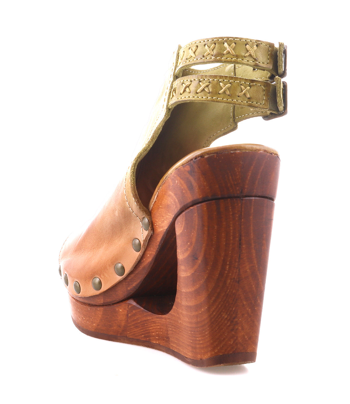 The Imelda sandal by Bed|Stü is a brown leather cutout wedge featuring light green adjustable ankle buckles, metal stud accents, and a wooden platform heel. Shown from a rear-side angle on a white background, this open-toe shoe highlights its unique silhouette.