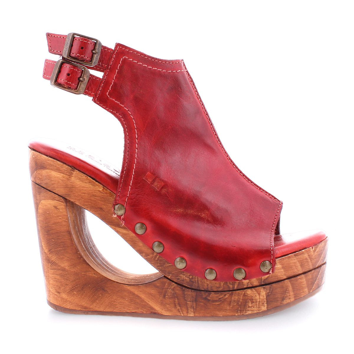 Introducing the Imelda wedge sandal by Bed|Stü, crafted in rich red leather with adjustable ankle buckles and adorned with brass studs along the sides. A chunky wooden heel showcases a striking cutout wedge detail, while the open-toe design delivers an effortlessly chic finish.