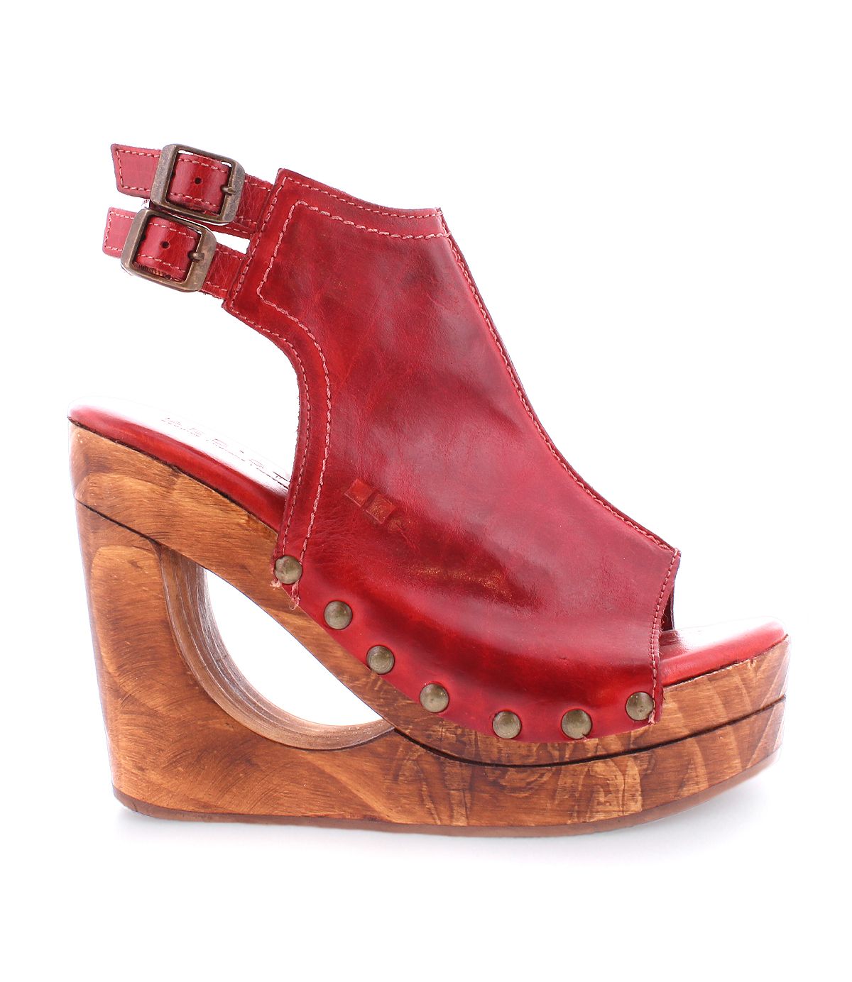 Introducing the Imelda wedge sandal by Bed|Stü, crafted in rich red leather with adjustable ankle buckles and adorned with brass studs along the sides. A chunky wooden heel showcases a striking cutout wedge detail, while the open-toe design delivers an effortlessly chic finish.