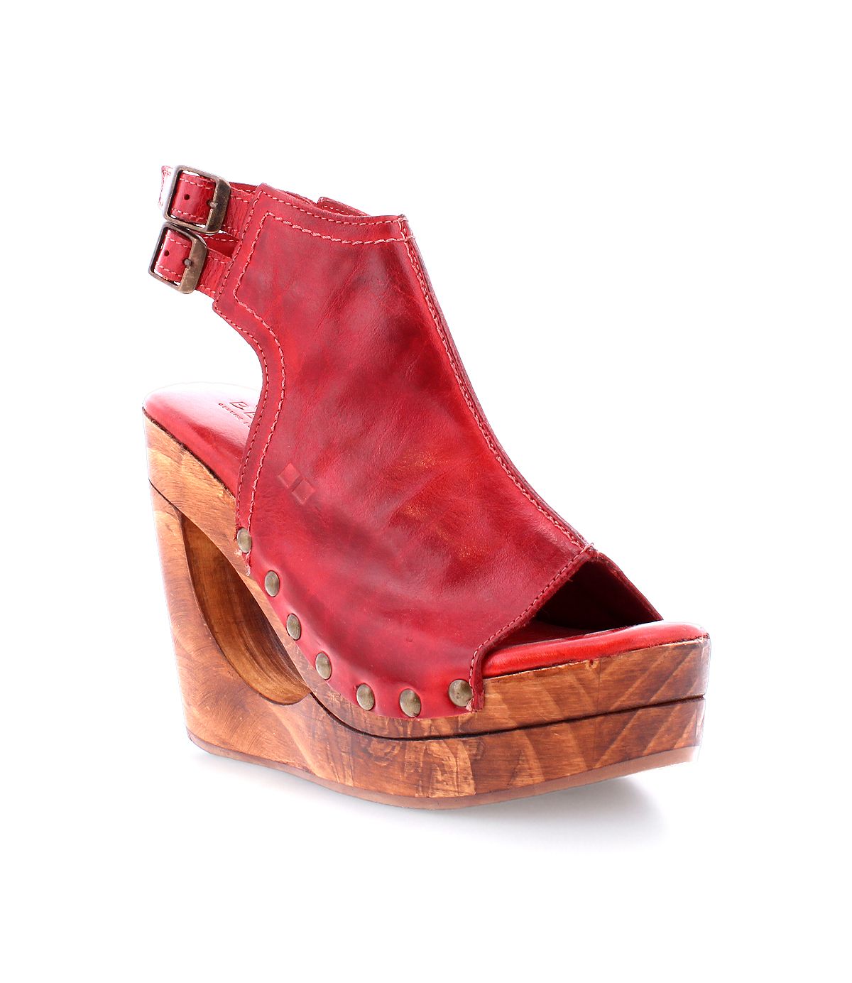 The Bed|Stü Imelda is a red leather open-toe wedge sandal featuring a bold cutout wedge design, wooden platform sole, metal stud accents, and an ankle strap with two adjustable buckles, shown against a white background.