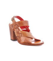 The Bed|Stü Intersection is a tan leather heeled sandal showcasing stylish crossover straps, a thick block heel, open-toe design, and an adjustable ankle strap, set against a white background.