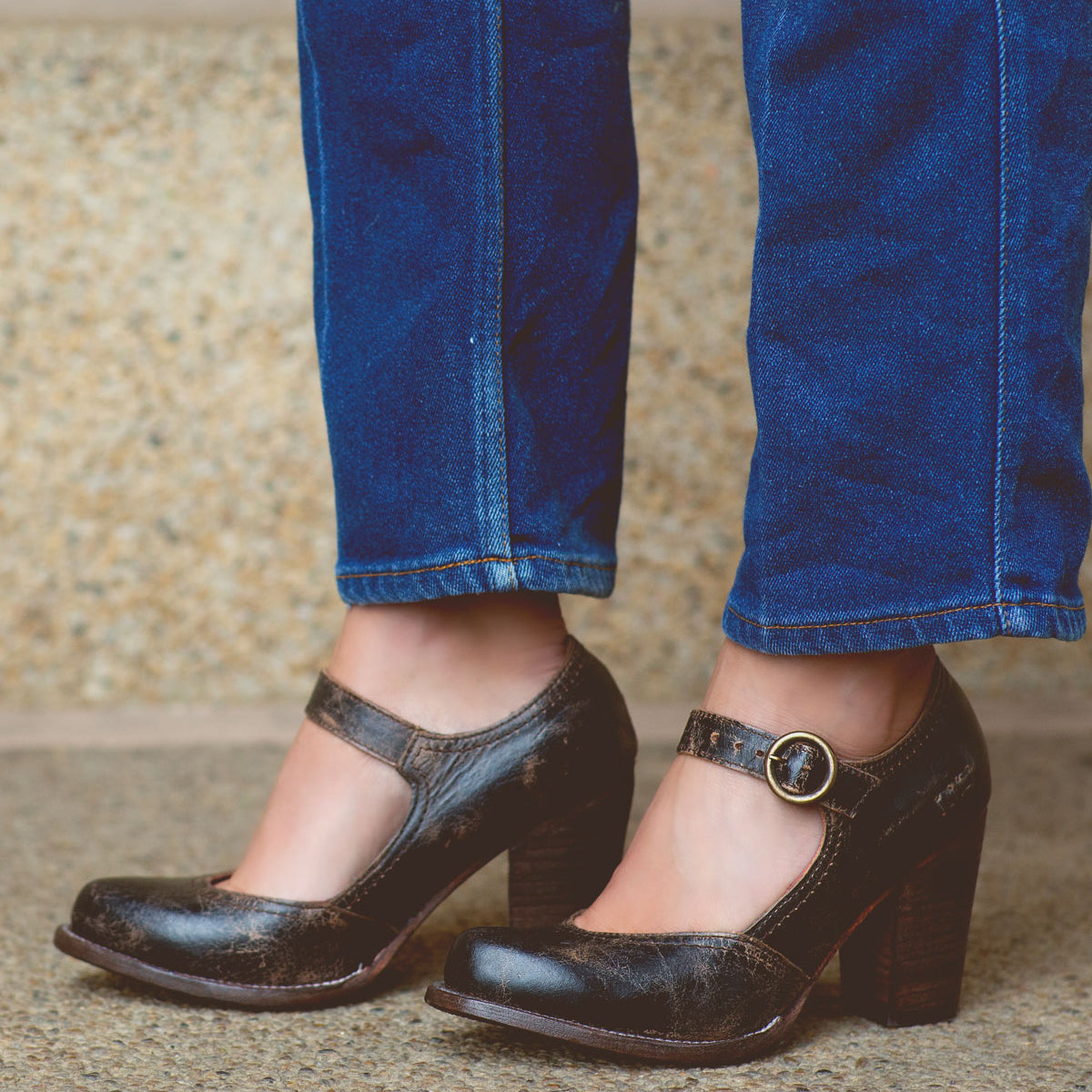 A person wearing blue jeans stands on a stone surface, showcasing the Bed|Stü Ishtar black Mary Jane pump high heel shoes with an adjustable strap.