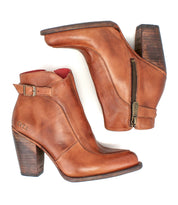 The Bed|Stü Isla is a pair of brown smooth leather ankle boots with block heels, side zippers, and buckle straps, displayed on a white background.