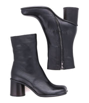 Two black Isodora ankle boots by Bed|Stü, handcrafted in Italian leather with rounded toes, medium-height cylindrical heels, and side zippers. Shown from a side view and a bottom view against a white background, these boots feature durable Blake-stitched construction for refined style.