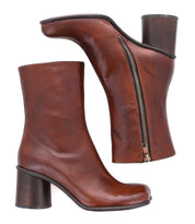 Two brown Isodora ankle boots by Bed|Stü, crafted from Italian leather with round toes, chunky high heels, and side zippers, are displayed—one standing upright and the other lying on its side to highlight the zipper—emphasizing the quality craftsmanship of Bed|Stü’s Italian leather boots.