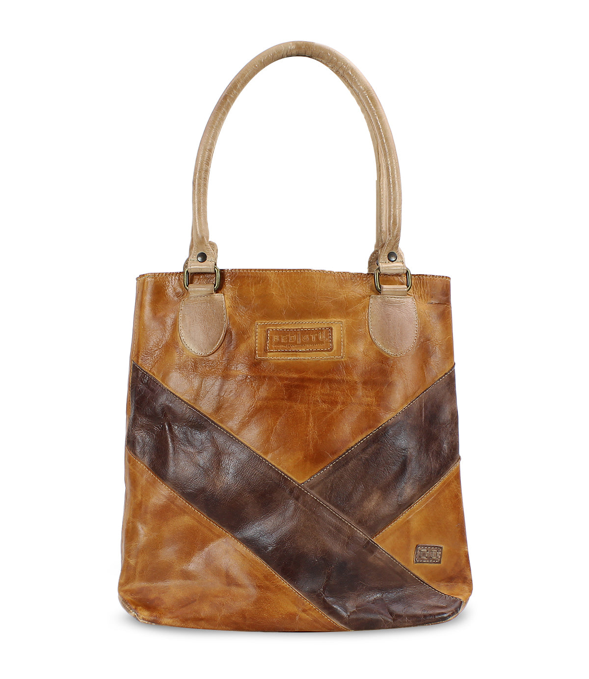 The Bed|Stü Italic is a brown leather tote bag with two handles, accented by diagonal dark brown and tan details, featuring an organic cotton lining and displayed against a white background.