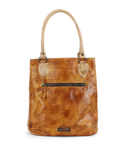 Bed|Stü's Italic tote is crafted from tan leather with dual handles, padded shoulder straps, a front zippered pocket, visible stitching, and a subtly distressed finish. Its spacious interior is lined with organic cotton, and the bag stands upright against a white background.
