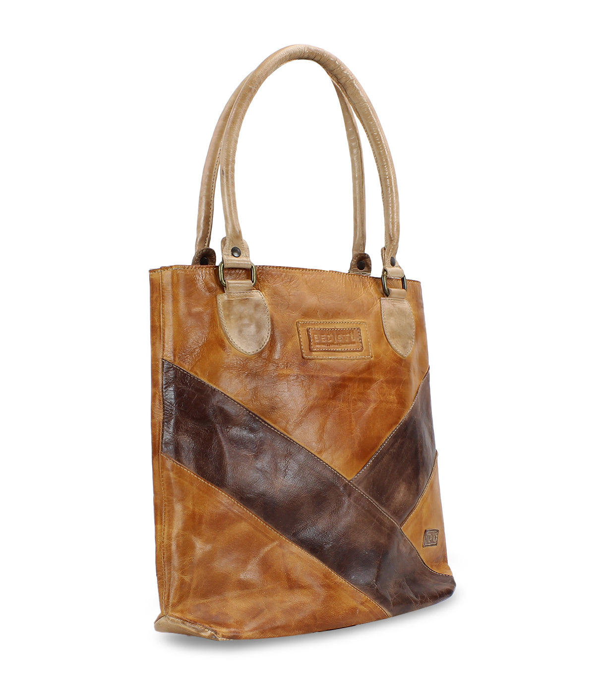 The Bed|Stü Italic is a brown leather tote bag with double handles, showcasing diagonal dark brown and tan panels and a rectangular stitched patch on the front. Designed for comfort, it features padded shoulder straps and stands upright against a white background.