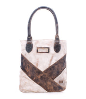 Introducing the Italic tote bag by Bed|Stü: a beige and brown leather handbag with two handles, highlighted by a diagonal brown stripe and a rectangular label on the front. This stylish accessory features padded shoulder straps for enhanced comfort and an organic cotton lining, ensuring a touch of sustainable luxury.