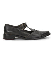 The Bed|Stü Jenny is a single black leather T-bar shoe with a buckle strap and low heel, featuring a cushioned insole for added comfort, shown in profile on a white background.