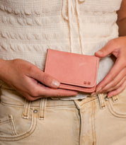 A person in a white top and beige pants holds the Bed|Stü Jeor compact wallet with both hands in front of their waist.