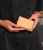 A person wearing a dark garment holds the Jeor compact card wallet by Bed|Stü with both hands against a neutral background. This small, rustic leather accessory features convenient credit card slots, seamlessly blending style and practicality in an understated design.