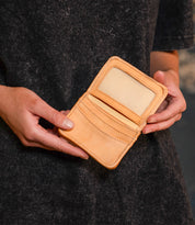A person wearing a dark textured shirt holds the Bed|Stü Jeor, an open rustic leather card wallet featuring multiple credit card slots and a clear ID window.