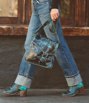 Wearing Bed|Stü’s Judgement cap toe lace-up shoes in teal, the person in cuffed blue jeans walks while carrying a blue and black satchel.