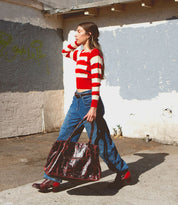 Wearing the "Judgement" block heel red shoes by Bed|Stü, a person in a red and white striped sweater, blue jeans, and carrying a large dark red bag walks outside.
