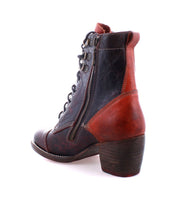 The Bed|Stü Judgement is a black and brown leather lace-up boot featuring a cap toe, side zipper, visible stitching, and a chunky block heel, shown against a white background.