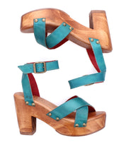 The Kalah by Bed|Stü is a pair of women’s wooden platform sandals with teal leather straps and brass buckles, featuring an adjustable ankle strap and a sustainably sourced wooden platform heel, displayed against a white background.