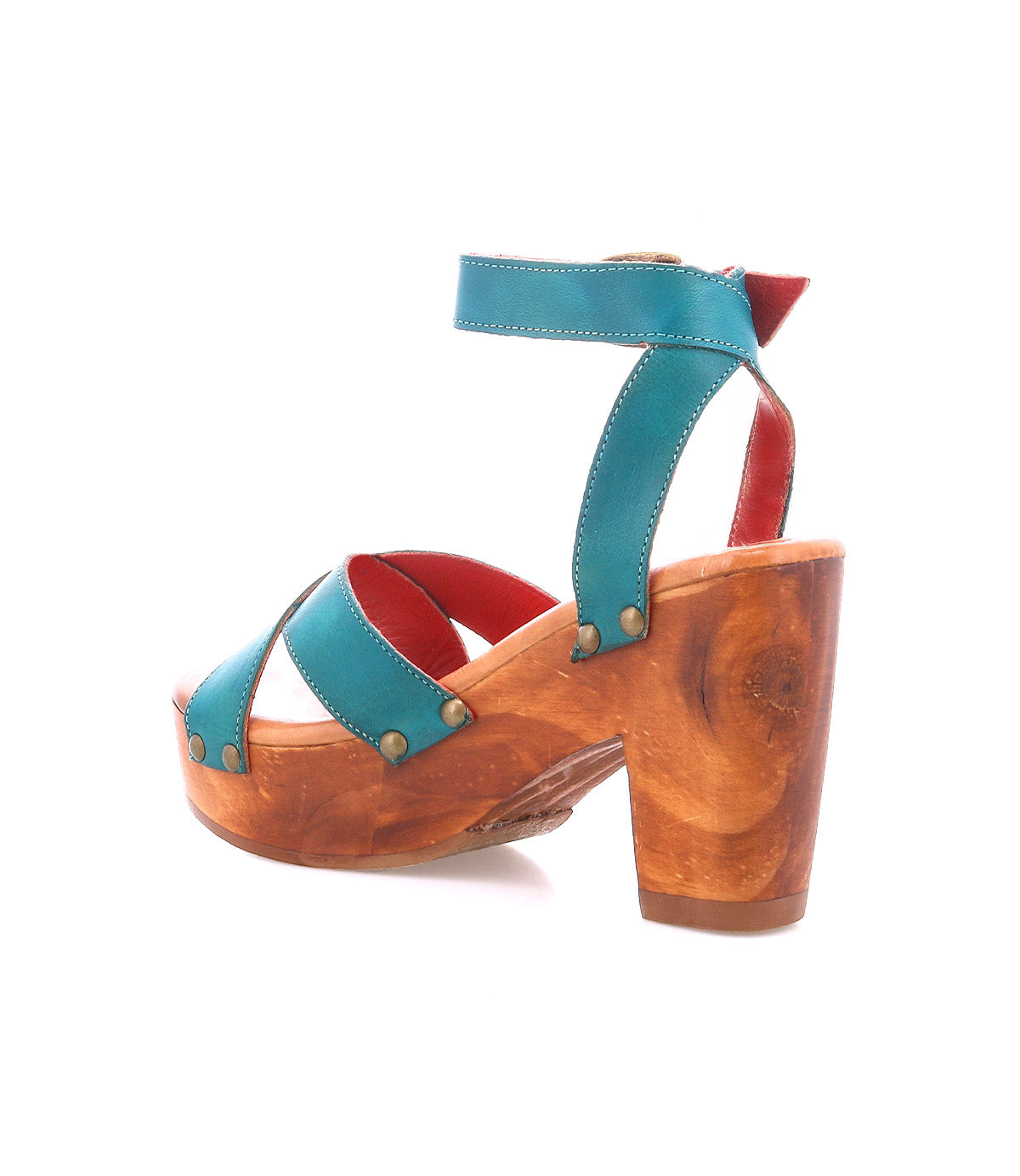 The Bed|Stü Kalah is a single teal sandal, featuring a chunky, sustainably sourced wooden heel, adjustable ankle strap, metal rivets, and striking red interior detailing, shown in a side view.