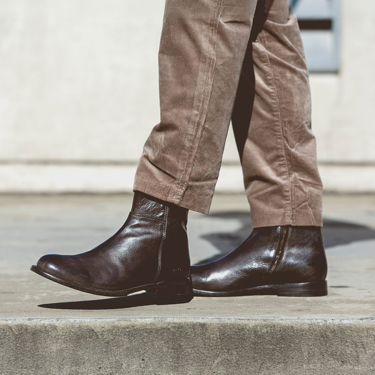 Wearing the Bed|Stü Kaldi brown leather ankle boots and beige corduroy pants, a person walks on a concrete sidewalk.